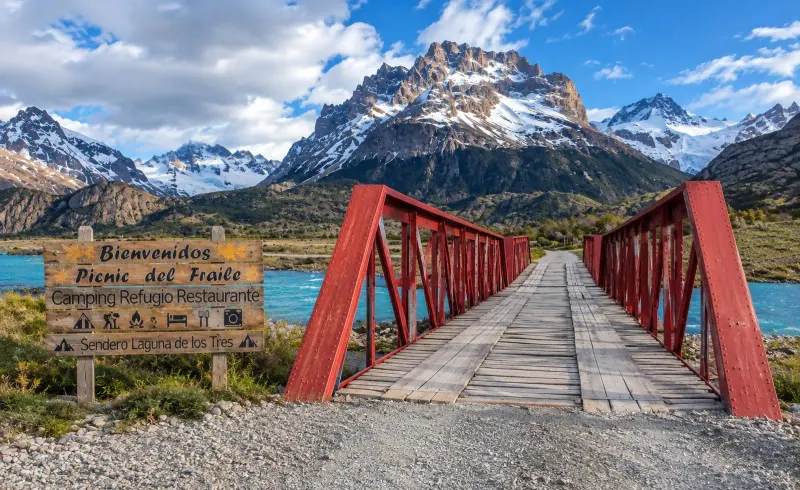 Puente rojo sobre el Río Eléctrico con montañas nevadas de fondo